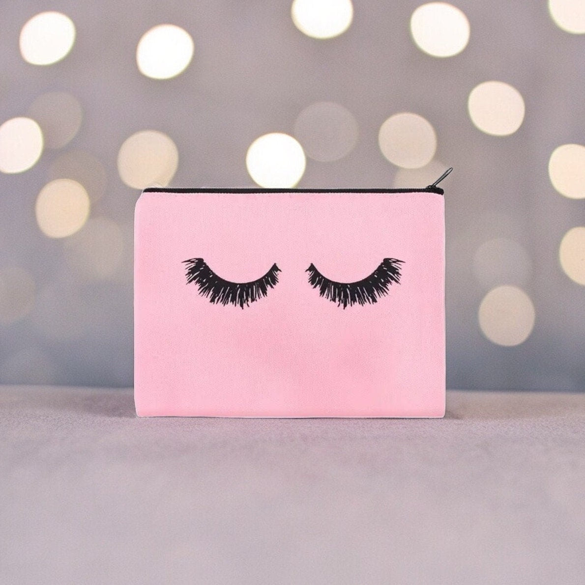 pink cosmetic zipper back with black lashes on a round lights shiny background